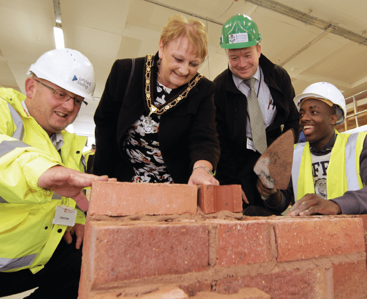 employees posing with mayor laying bricks